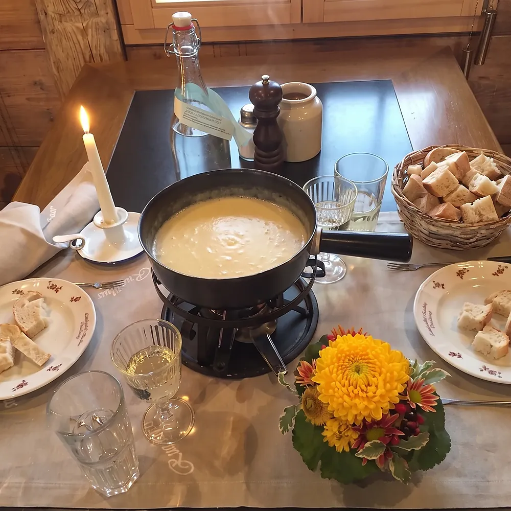 Fondue mit Brotwürfeln, Kerze und Blumen auf dem Tisch